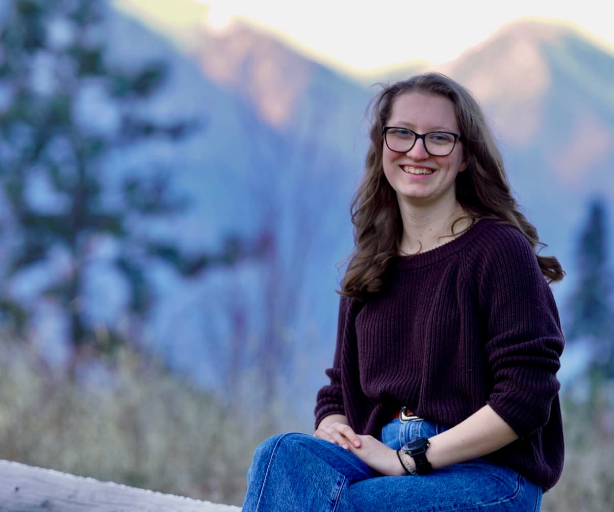 Leah, founder of Dream Baby Newborn Care, smiling outdoors in front of a mountain landscape